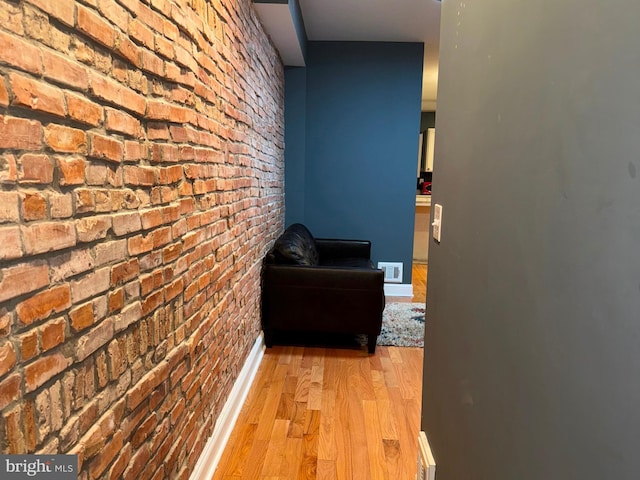 corridor featuring brick wall and light hardwood / wood-style flooring