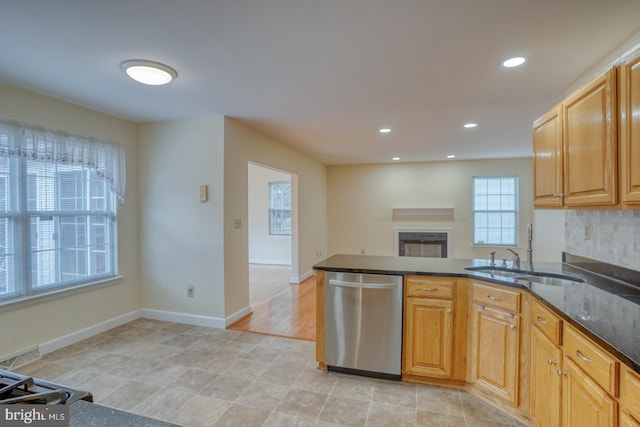 kitchen with kitchen peninsula, decorative backsplash, stainless steel dishwasher, dark stone counters, and sink