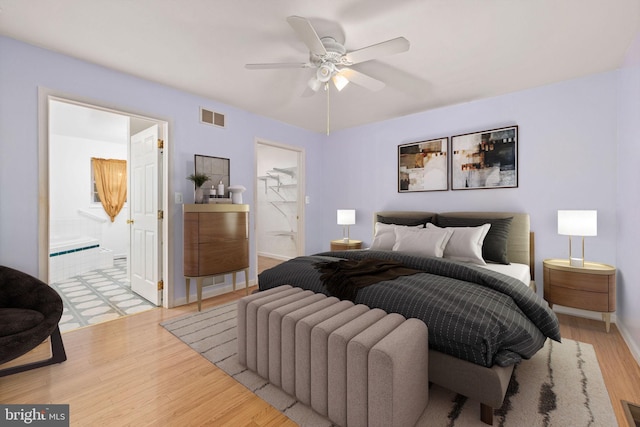 bedroom with light wood-type flooring, a closet, a walk in closet, and ceiling fan