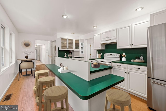 kitchen with light hardwood / wood-style flooring, white cabinetry, stainless steel refrigerator, white electric range, and a kitchen breakfast bar