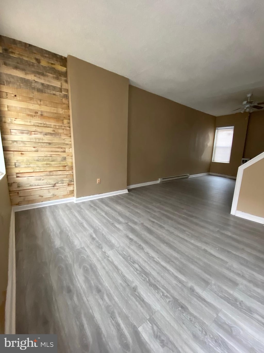 unfurnished living room featuring ceiling fan, a baseboard radiator, wood walls, and hardwood / wood-style floors