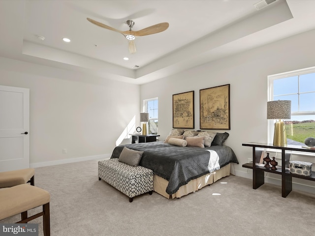 bedroom with light carpet, ceiling fan, and a tray ceiling