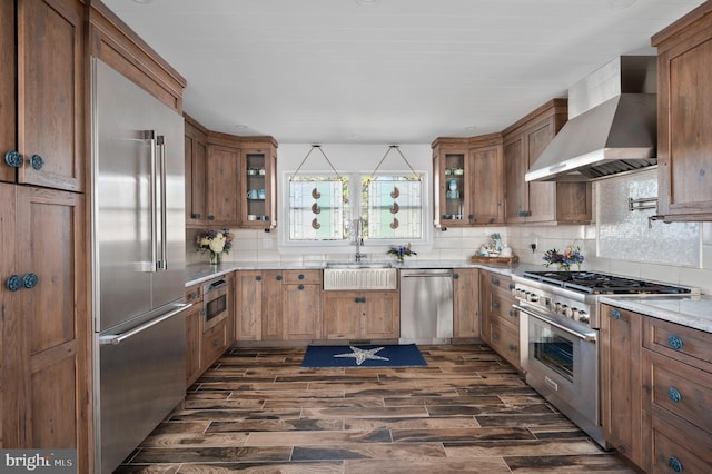 kitchen featuring decorative backsplash, wall chimney exhaust hood, high end appliances, sink, and dark hardwood / wood-style flooring