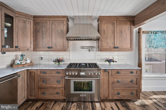 kitchen featuring wall chimney range hood, light stone counters, appliances with stainless steel finishes, and dark wood-type flooring