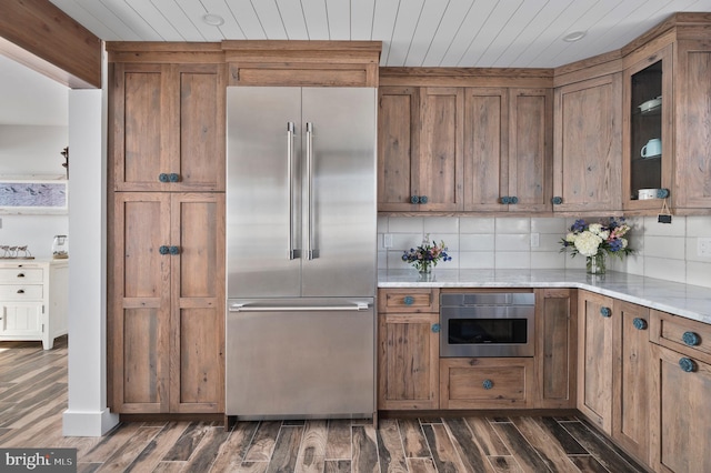 kitchen featuring appliances with stainless steel finishes, tasteful backsplash, light stone countertops, and dark wood-type flooring