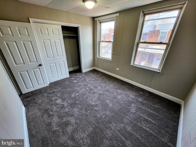 unfurnished bedroom featuring wood walls, dark carpet, and a closet