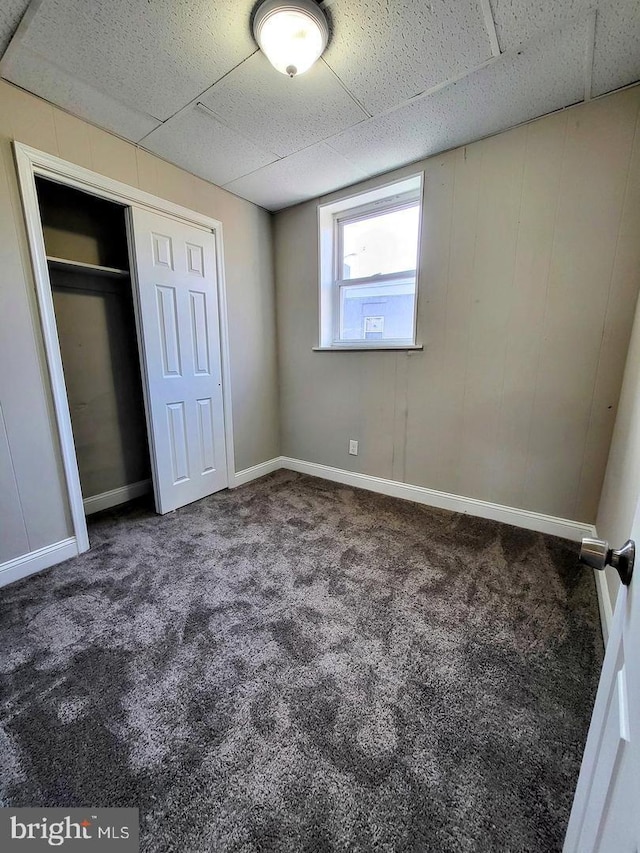 unfurnished bedroom with carpet, a drop ceiling, and a closet