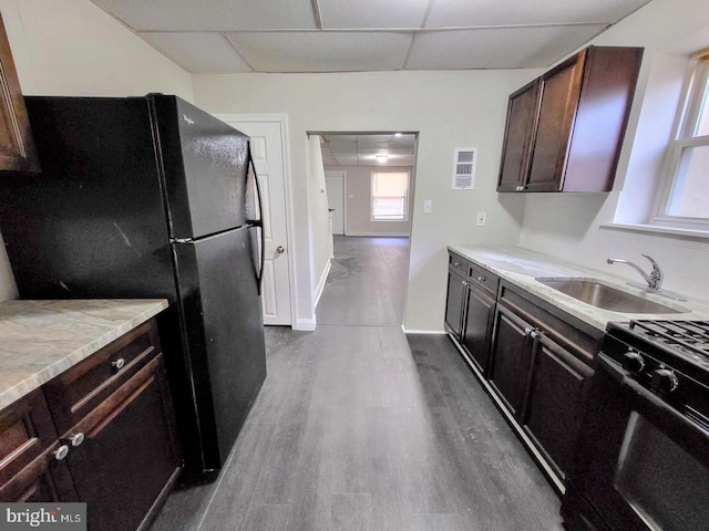 kitchen featuring a paneled ceiling, hardwood / wood-style floors, black refrigerator, sink, and range with gas cooktop