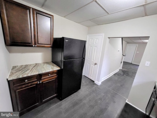 kitchen with a paneled ceiling, dark brown cabinetry, and black refrigerator