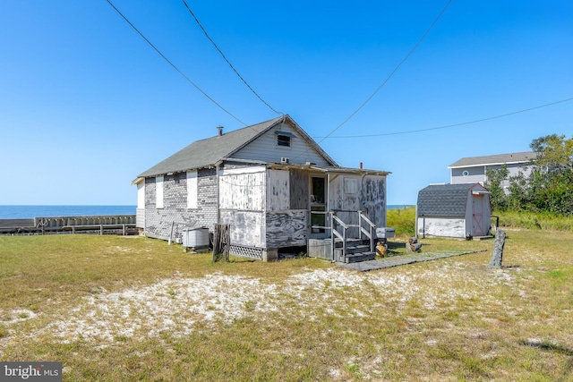 rear view of property with a shed, a water view, and a yard