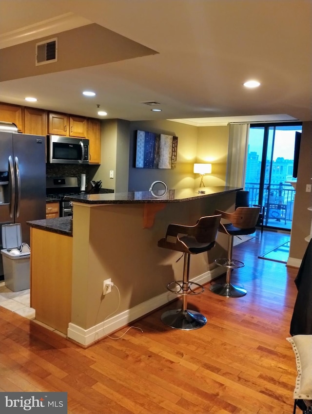 kitchen with kitchen peninsula, light hardwood / wood-style floors, dark stone countertops, and appliances with stainless steel finishes