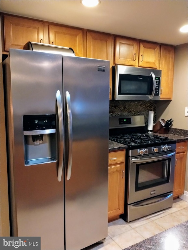 kitchen with stainless steel appliances, light tile patterned flooring, dark stone counters, and backsplash