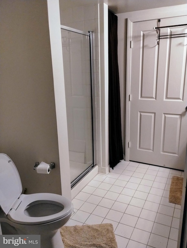 bathroom featuring tile patterned flooring, toilet, and a shower with shower door