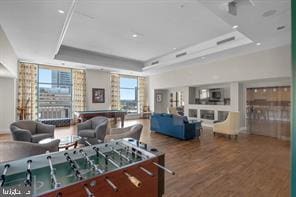 game room with wood-type flooring, a healthy amount of sunlight, and a raised ceiling