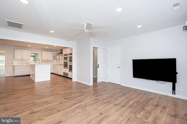 unfurnished living room featuring ceiling fan, light wood-type flooring, and sink