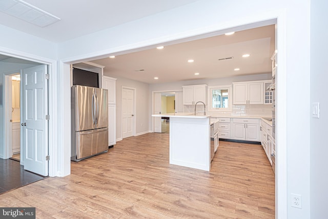 kitchen featuring light hardwood / wood-style floors, stainless steel refrigerator, a center island with sink, and white cabinets