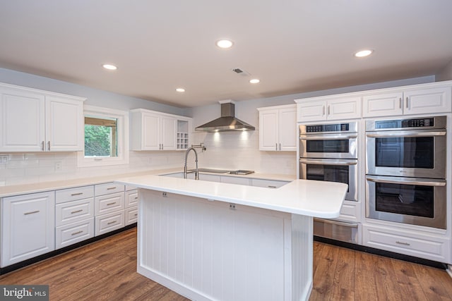 kitchen with white cabinets, stainless steel double oven, wall chimney exhaust hood, and dark wood-type flooring