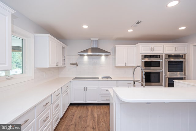 kitchen with stainless steel double oven, dark hardwood / wood-style floors, wall chimney range hood, and white cabinets