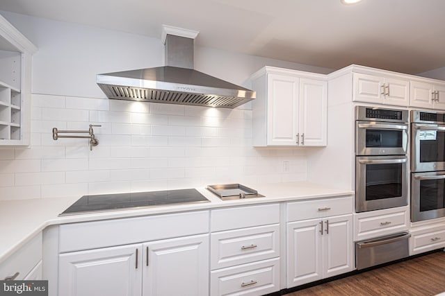 kitchen with black electric cooktop, white cabinetry, dark wood-type flooring, double oven, and wall chimney range hood