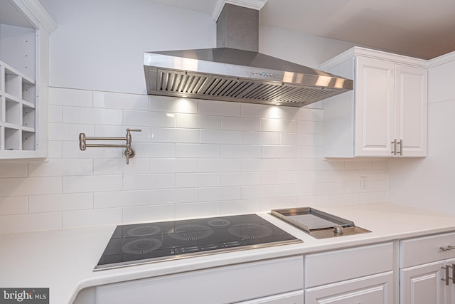 kitchen with decorative backsplash, black electric stovetop, white cabinetry, and wall chimney range hood