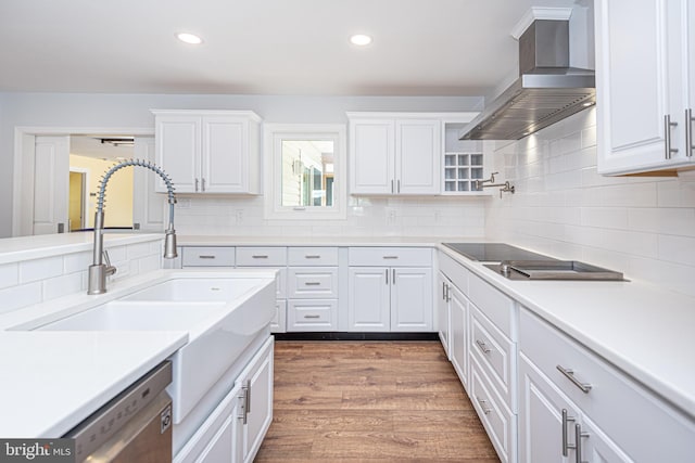 kitchen with decorative backsplash, white cabinets, wood-type flooring, stainless steel dishwasher, and wall chimney range hood