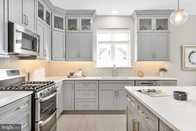 kitchen with appliances with stainless steel finishes, hanging light fixtures, backsplash, gray cabinets, and sink