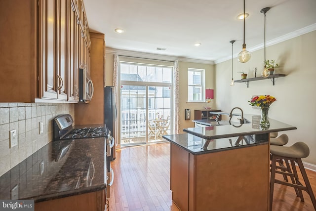 kitchen with dark stone countertops, pendant lighting, stainless steel appliances, and light hardwood / wood-style flooring