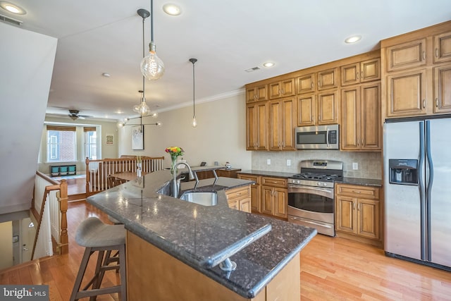 kitchen featuring light hardwood / wood-style floors, a kitchen island with sink, pendant lighting, sink, and appliances with stainless steel finishes