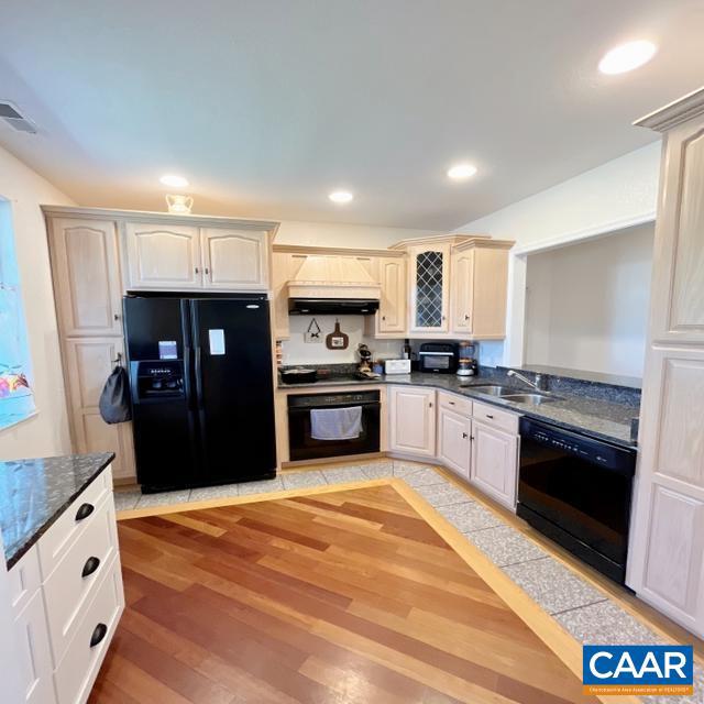 kitchen featuring dark stone countertops, black appliances, hardwood / wood-style floors, and sink