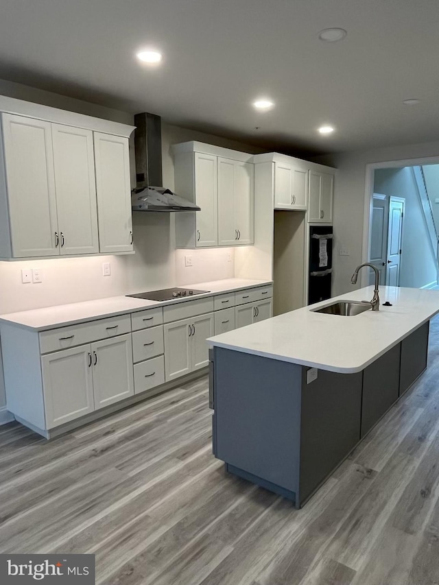 kitchen featuring a center island with sink, sink, white cabinetry, and wall chimney range hood