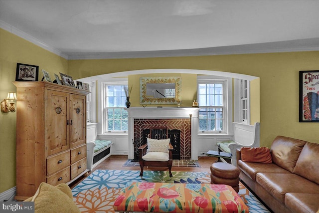 living room featuring wood-type flooring, ornamental molding, a tiled fireplace, and a wealth of natural light