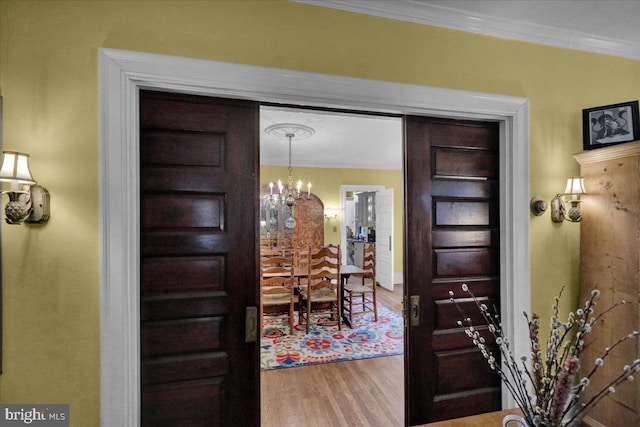 foyer entrance featuring wood-type flooring, ornamental molding, and a notable chandelier