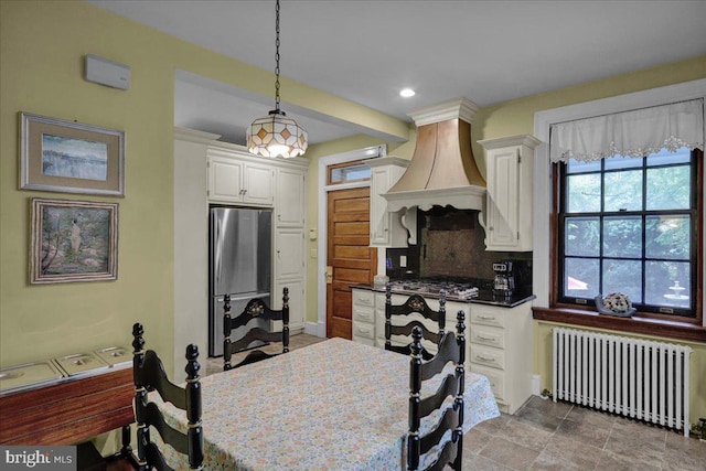 kitchen featuring white cabinets, hanging light fixtures, radiator heating unit, stainless steel appliances, and custom range hood