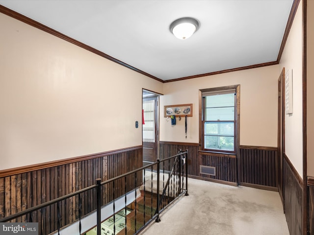 hallway featuring crown molding, wood walls, and light colored carpet