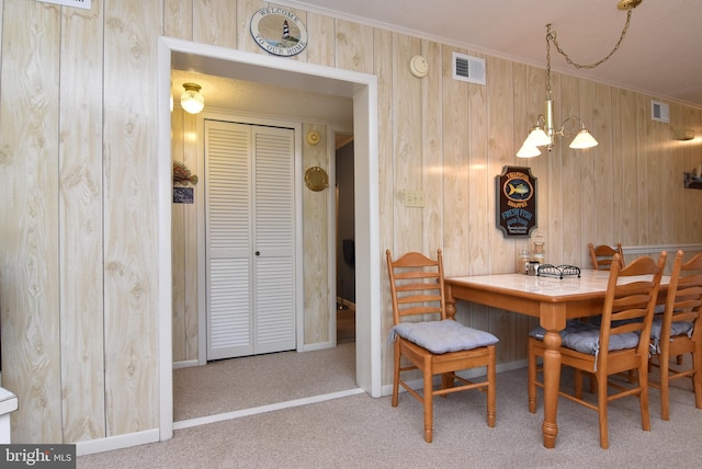 carpeted dining room featuring a notable chandelier, wood walls, and crown molding