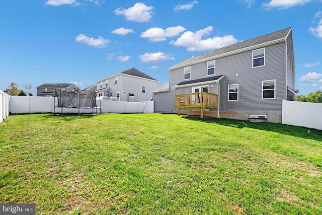 back of property with a yard, a deck, and a trampoline