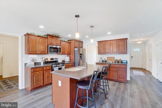 kitchen with hanging light fixtures, a kitchen island with sink, stainless steel appliances, a breakfast bar, and light hardwood / wood-style floors