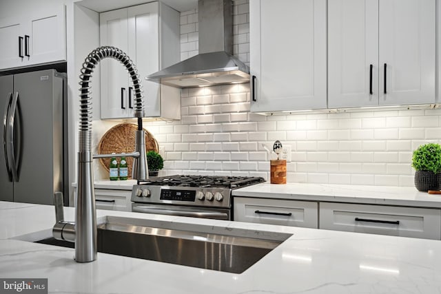 kitchen featuring light stone counters, white cabinets, wall chimney exhaust hood, backsplash, and stainless steel appliances