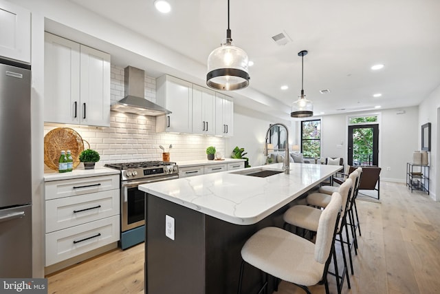 kitchen featuring white cabinets, sink, a center island with sink, wall chimney exhaust hood, and appliances with stainless steel finishes