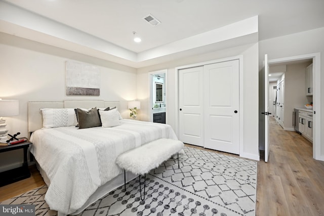 bedroom featuring light hardwood / wood-style floors, ensuite bath, and a closet