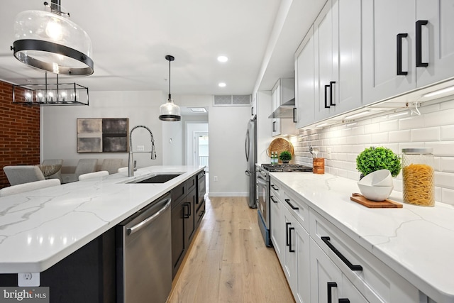 kitchen featuring light wood-type flooring, sink, white cabinets, stainless steel appliances, and decorative light fixtures