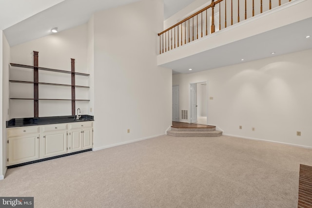 unfurnished living room featuring a towering ceiling, light colored carpet, and sink