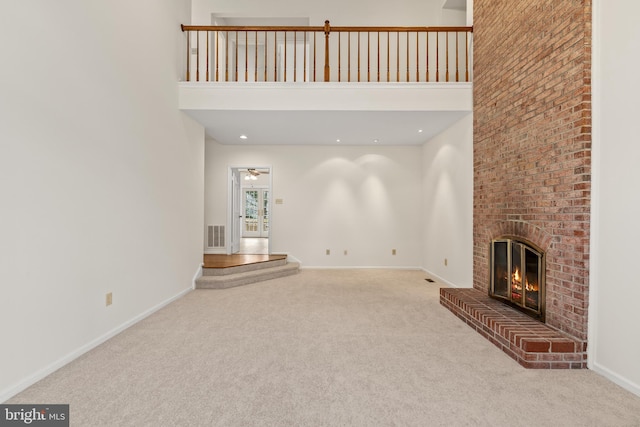 unfurnished living room with light carpet, a towering ceiling, a brick fireplace, and ceiling fan