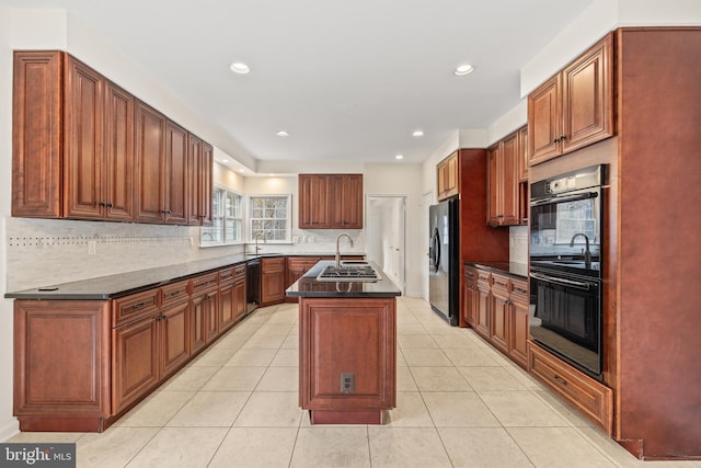 kitchen with decorative backsplash, sink, a kitchen island with sink, and black appliances