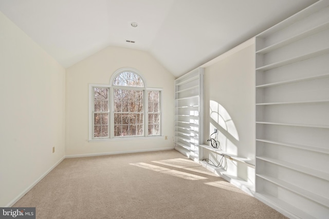 unfurnished room with built in shelves, light colored carpet, and lofted ceiling