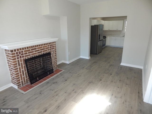 unfurnished living room featuring wood-type flooring and a brick fireplace