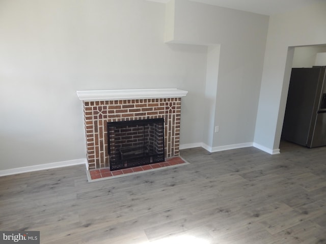 unfurnished living room featuring wood-type flooring and a brick fireplace