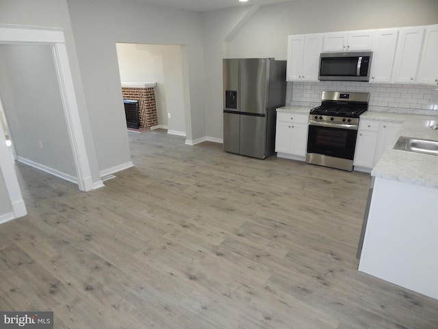 kitchen with white cabinets, stainless steel appliances, backsplash, and light hardwood / wood-style floors