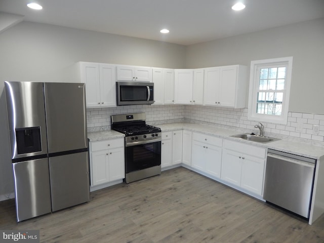 kitchen featuring light hardwood / wood-style flooring, sink, decorative backsplash, appliances with stainless steel finishes, and white cabinetry