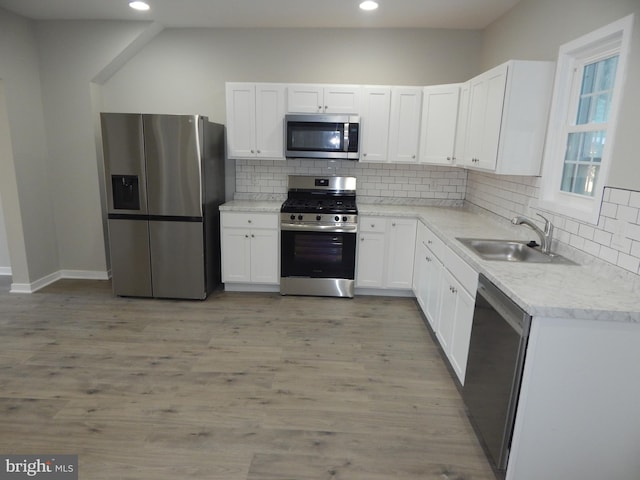 kitchen with light hardwood / wood-style floors, tasteful backsplash, sink, appliances with stainless steel finishes, and white cabinetry